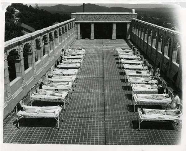 Una fotografía antigua muestra a pacientes de un hospital tomando el sol en una terraza.